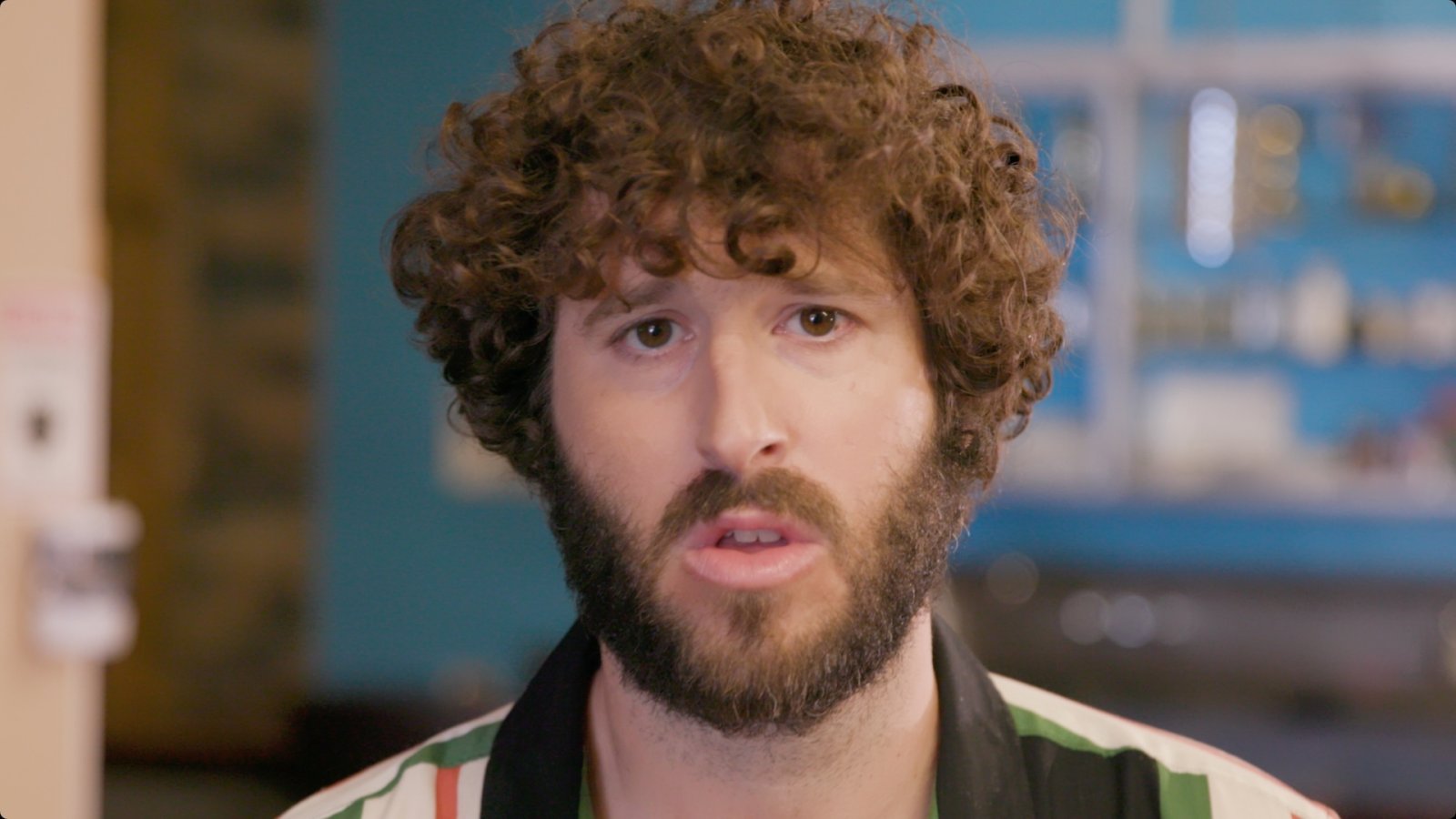 Close-up of a curly-haired man mid-sentence, talking to camera indoors