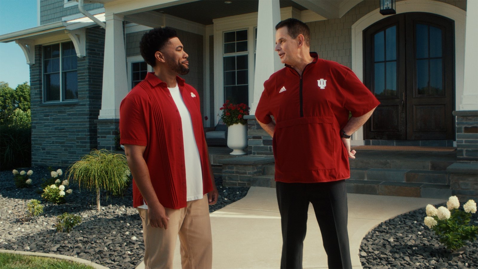 Coach Cignetti in a red Indiana quarter-zip talks with a man in a red shirt outside a suburban house