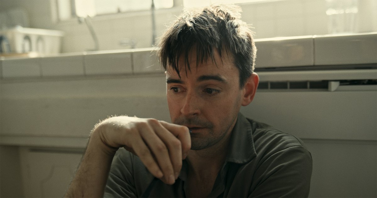 Man resting his chin on his hand, looking down pensively in a sunlit kitchen