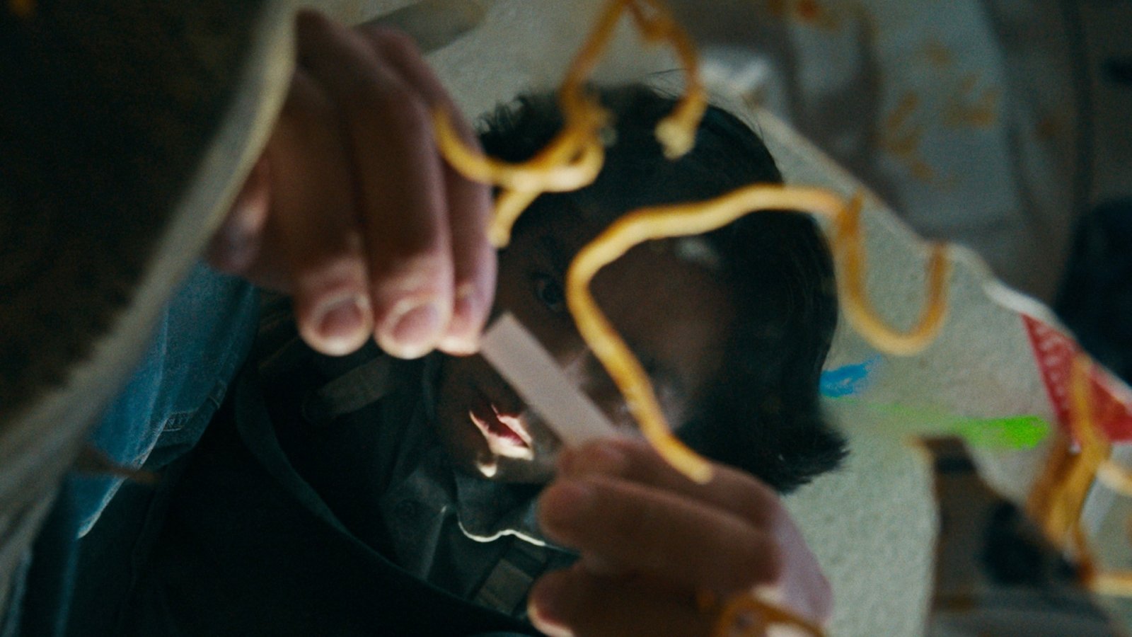 Close-up of a child’s face tangled in yellow noodle-like strands hanging from above