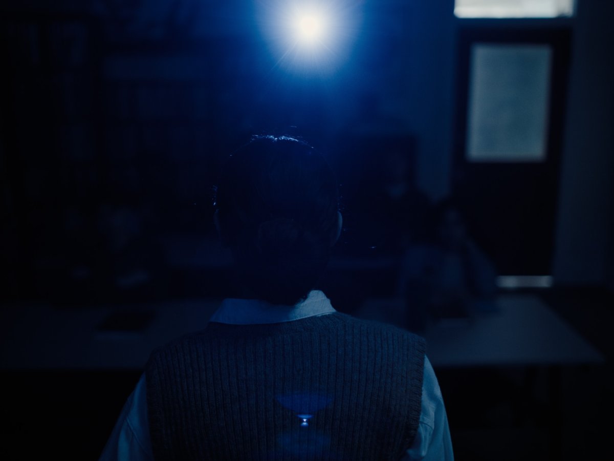 Silhouette of a man seen from behind in a dim blue-lit room, a bright light glowing overhead