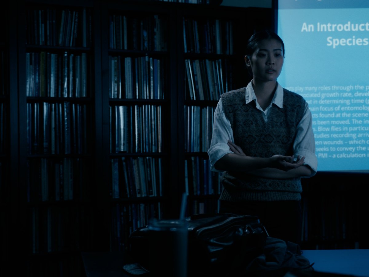 Woman with arms crossed presenting in front of a bookshelf and projector screen reading "An Introduction"