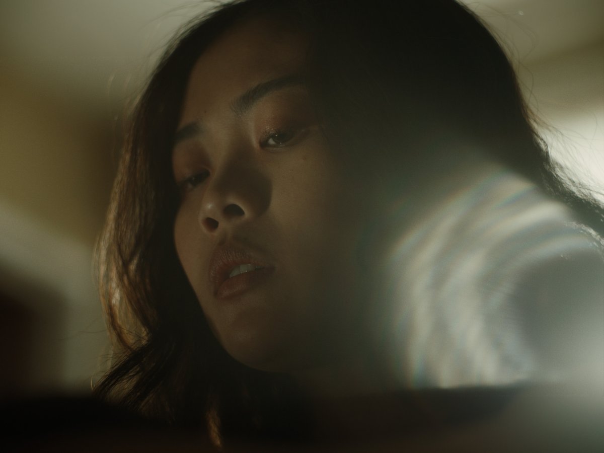 Extreme close-up of a woman’s face looking down, soft window light behind her