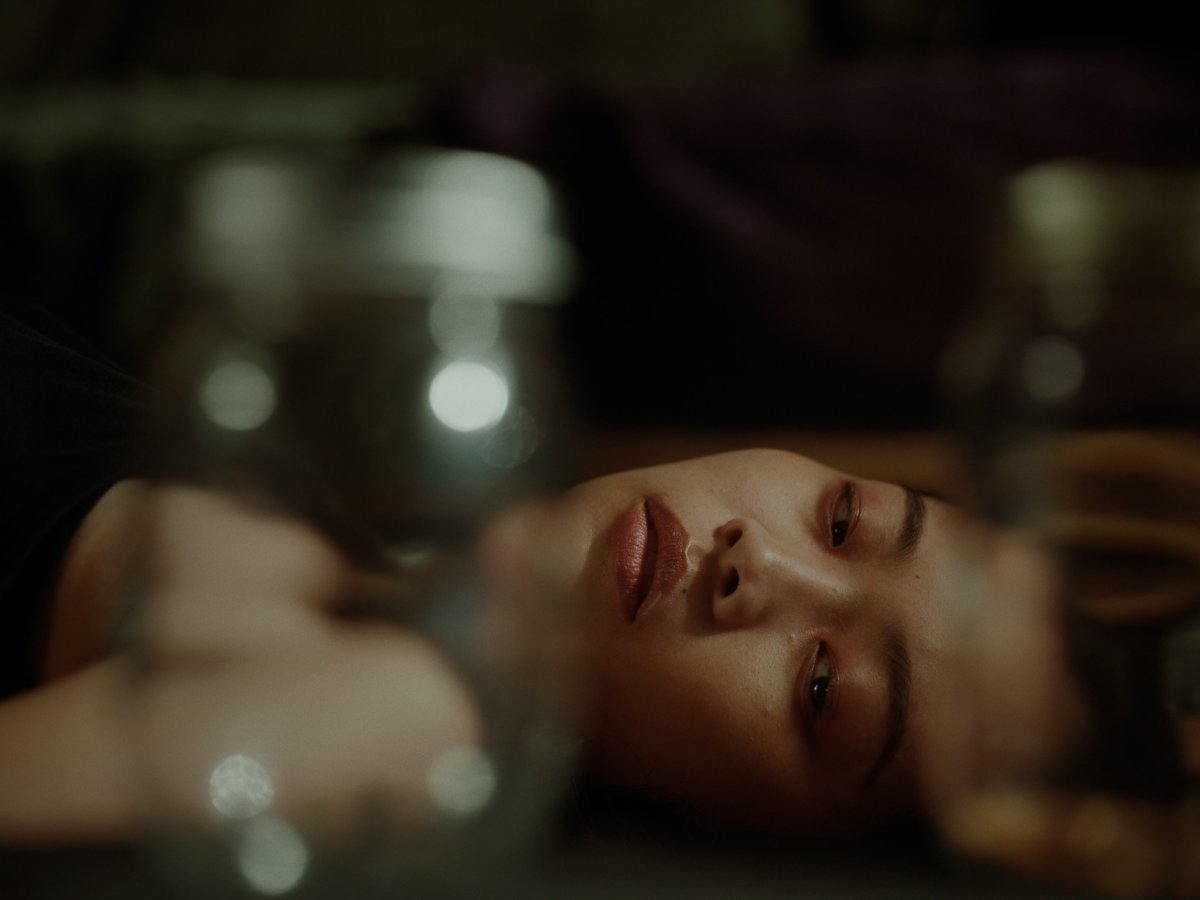 Close-up of a woman lying down with parted lips, candlelight glowing softly behind her