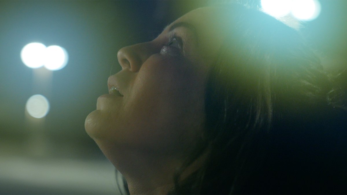 Close-up profile of a woman’s face looking up, lit by blurred streetlights at night