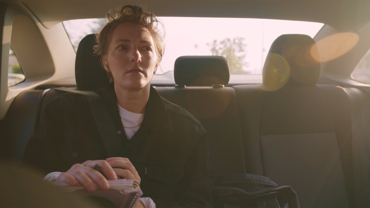 Woman in the back seat with tousled hair looking out the window, backlit by bright sunlight