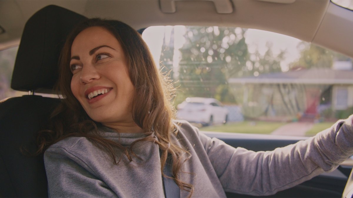 Smiling woman driving with her arm out, glancing back over her shoulder